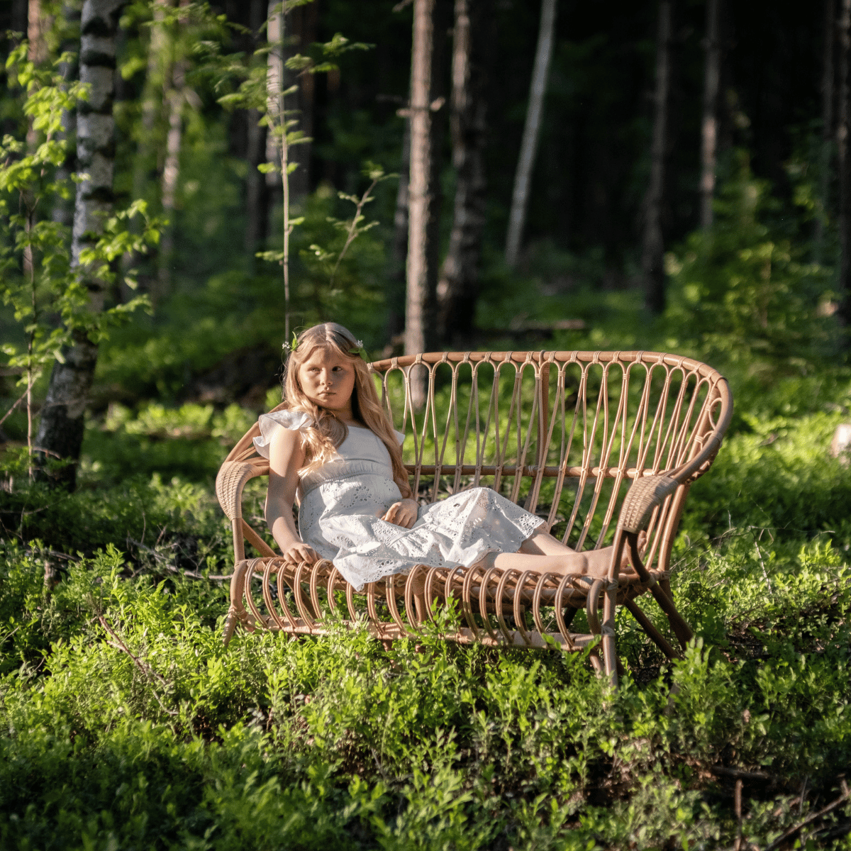 Tyttö istuu kesäisessä metsässä lumikenkäsohvalla